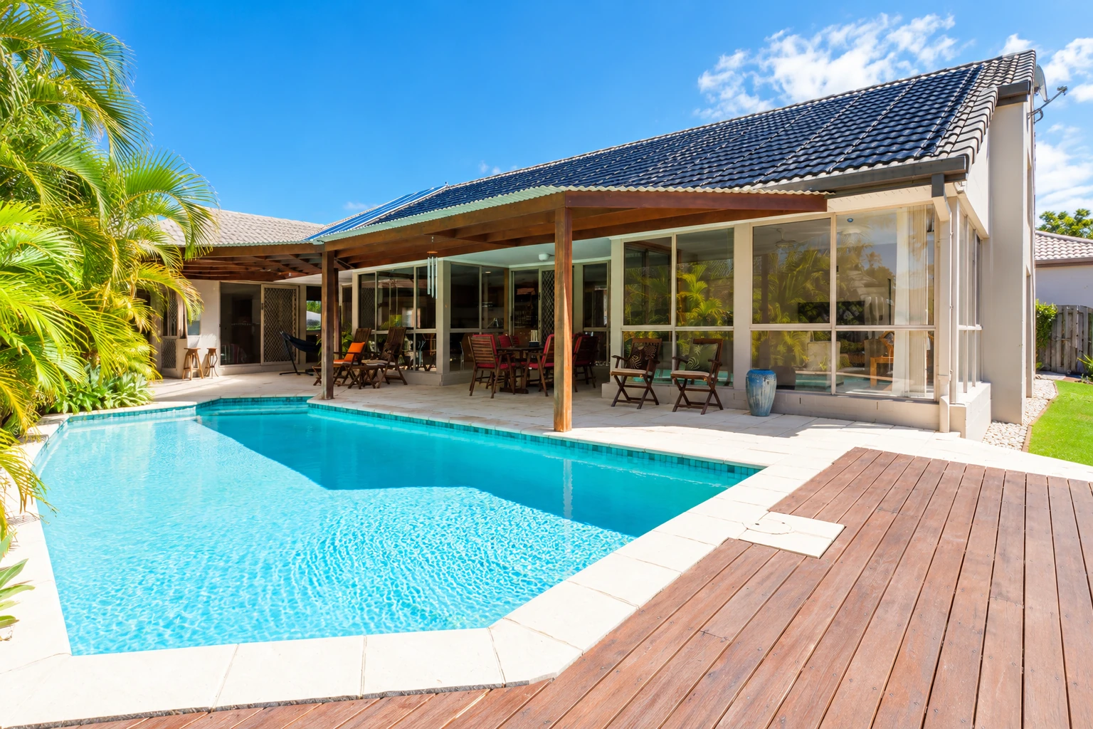 Wooden patio cover shelters seating beside a glass-enclosed room and swimming pool.