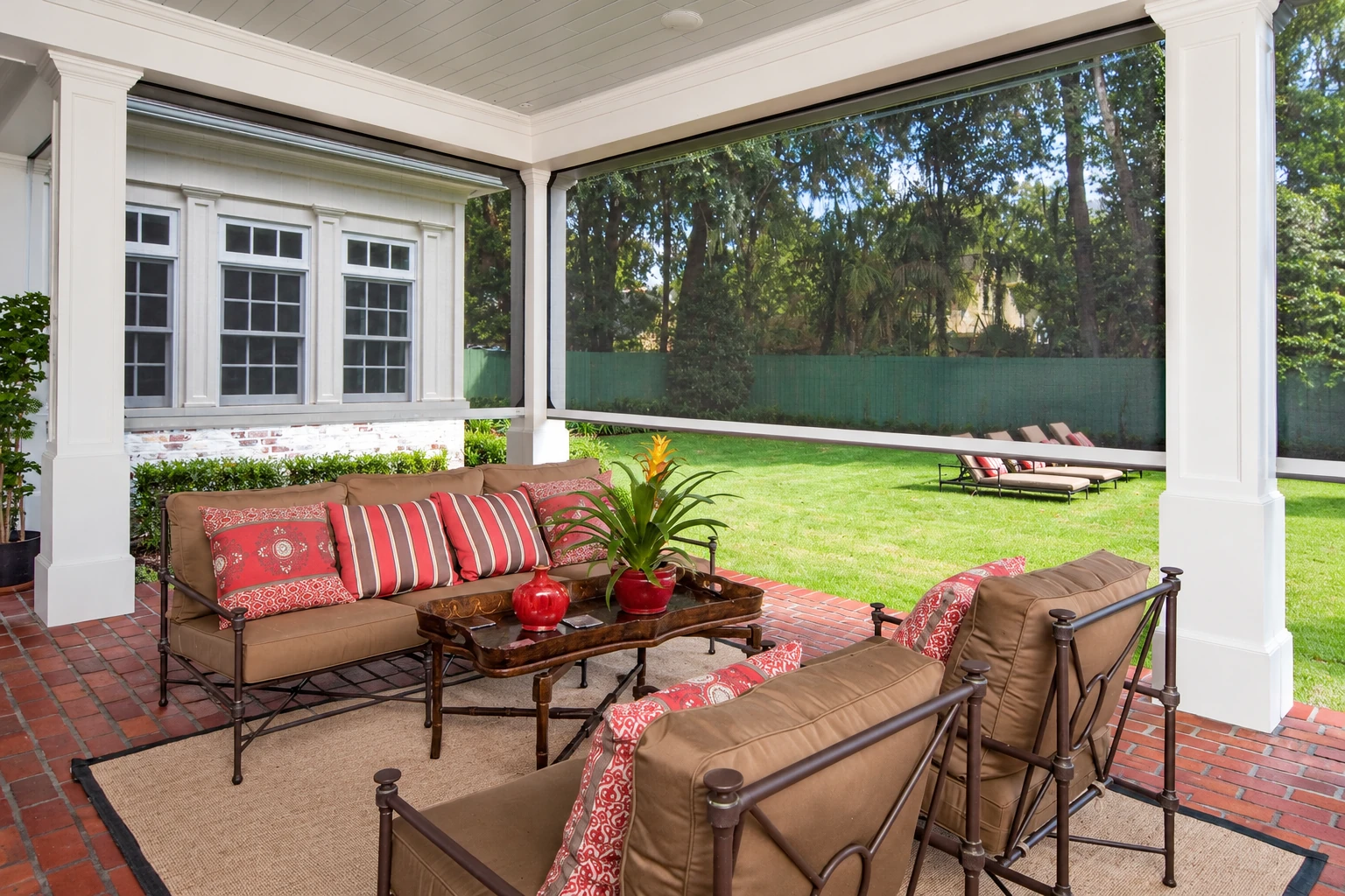 Covered patio with white columns, dark screening, brick flooring, and cushioned seating facing a garden.