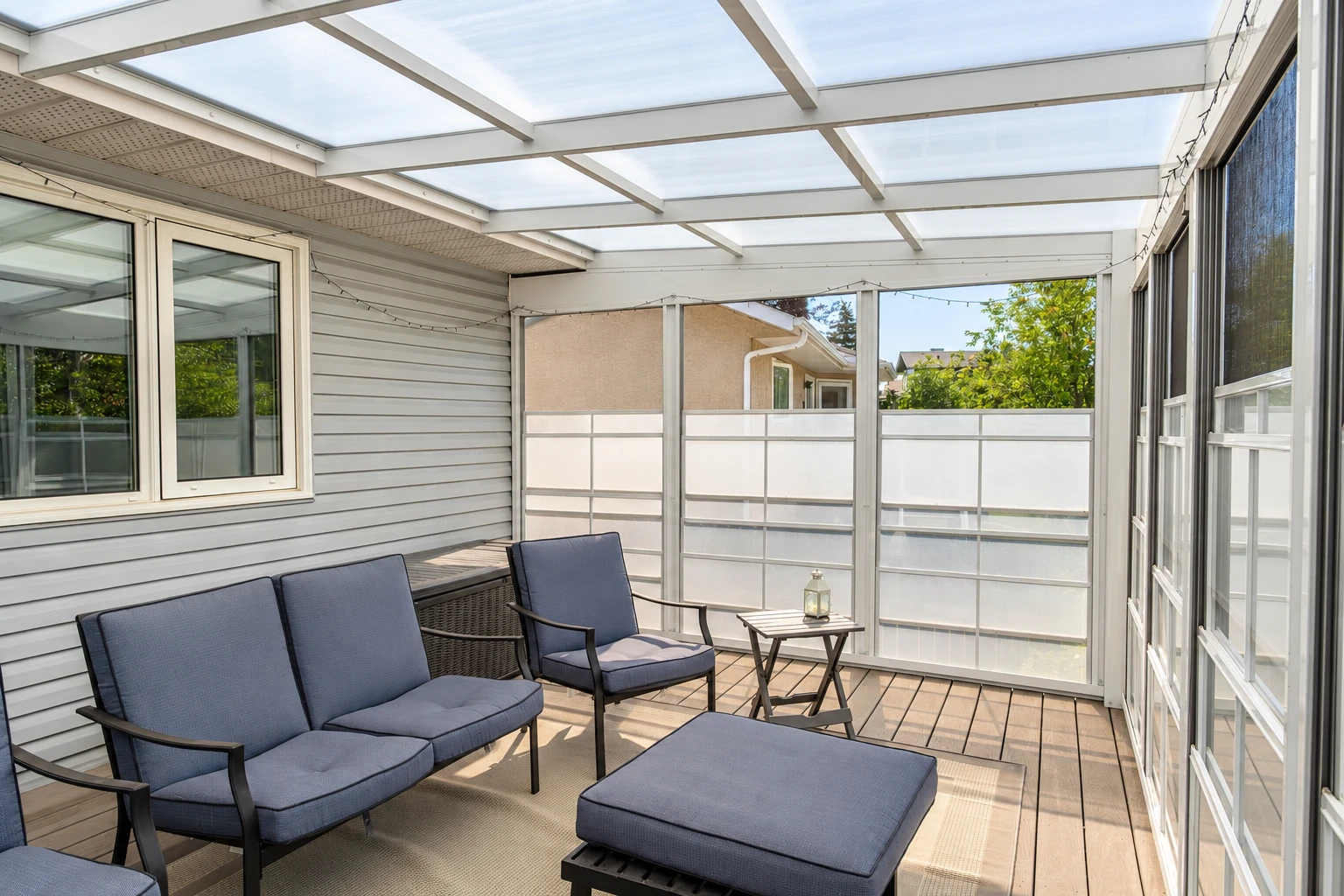 Sunroom addition with a translucent paneled roof, screened windows, and blue-cushioned patio seating.
