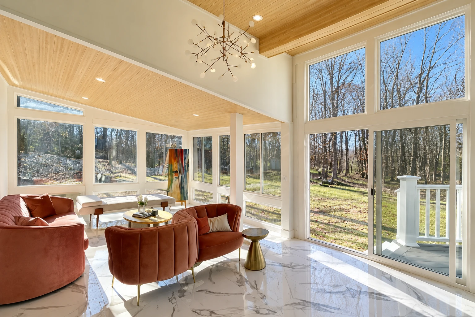 Sunroom with tall white-framed windows, a wood-paneled ceiling, marble-look floor and rust-colored seating.