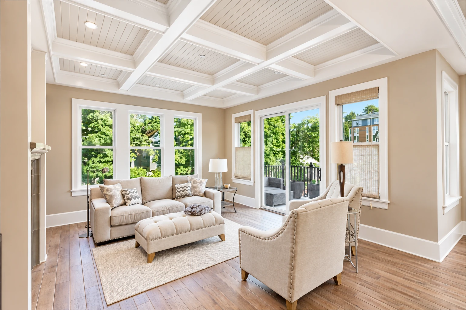Bright sunroom living area with beige seating, wood-look floors, large windows, and a white coffered ceiling.